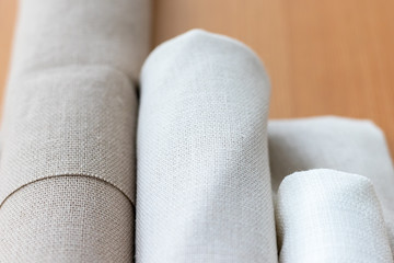 Three rolls of natural linen fabric in different colors on a wooden table. Selective focus. Closeup view. Blurred background