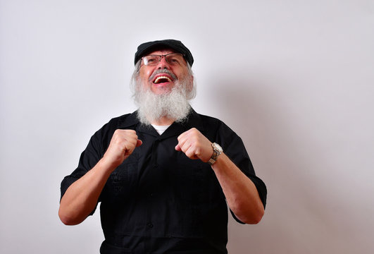 A very happy old man is laughing and in great spirit. .. .Mature gentleman with a newsboy cap and black guayabera shirt and long white beard..