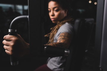selective focus of attractive african american girl with tattoo exercising on gym machine