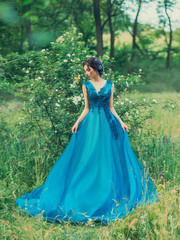 Mysterious girl holds dress both hands. green forest. shrub white flowers blue puffy lace evening...