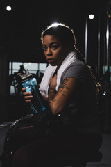 young african american girl with tattoo holding sports bottle in gym