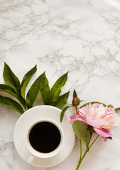 White cup of coffee or tea and one pink peony on a decorative marble table surface. Beautiful morning or coffee break with hot drink and spring flower. International Womans day concept, card design