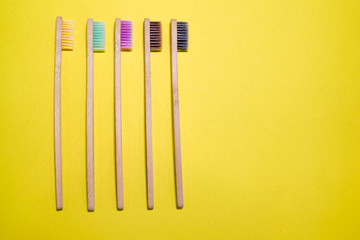 Eco bamboo toothbrashes with multicolored bright bristles on yellow background 