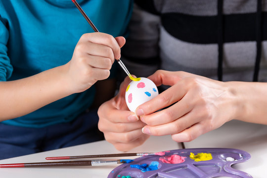 Mother and her child hands painting Easter eggs. A mother helps her son paint an egg with a paintbrush at home. Happy family preparing for Easter. Easter holiday concept