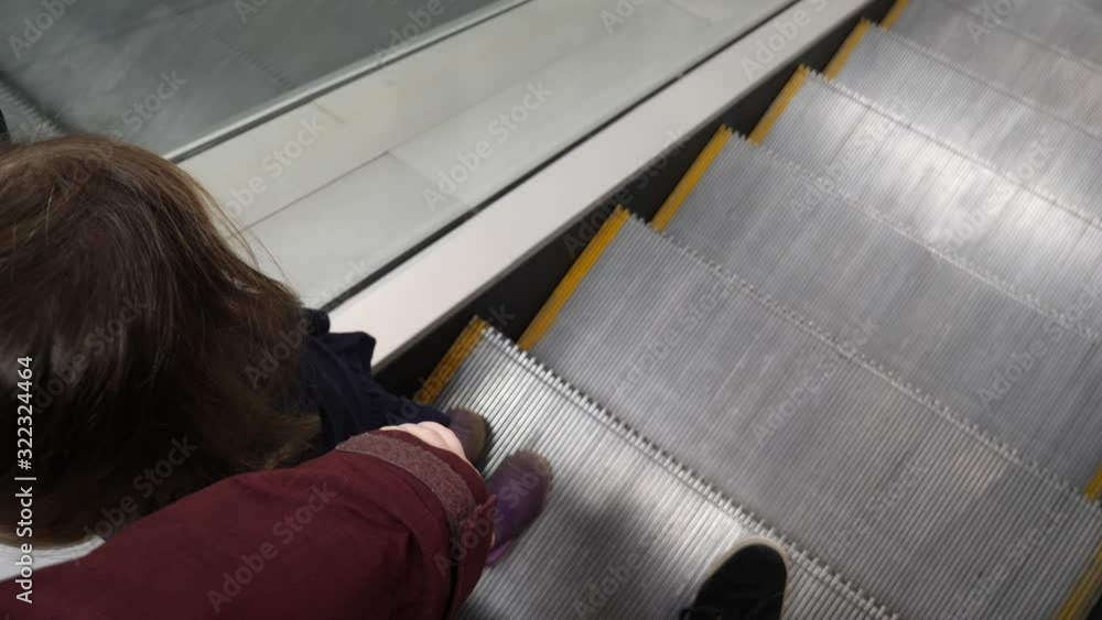 Poster parent holding the hand of a child while riding an escalator down - looking down point of view