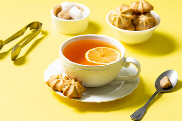 Tea with lemon in a white Cup and lemon cookies with poppy seeds in a white ceramic bowl on a yellow background. The concept of Breakfast or snack