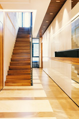 Bright modern hall with glossy surfaces, wooden staircase, ladder ceiling with lights and tiles floor