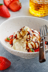Gourmet burrata cheese with strawberry tartare with mint, honey and balsamic in a light plate on a gray concrete or stone background. Breakfast.  Mediterranean (Italian) cuisine. Selective focus
