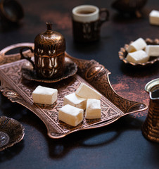 Turkish delight or lokum served in traditional oriental copper serving set. Turkish sweets, coffee in cezve and cup. Dark background, close up