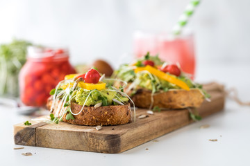 Two pieces of avocado toast on a wooden board ready for eating with a glass of fresh kombucha in behind.