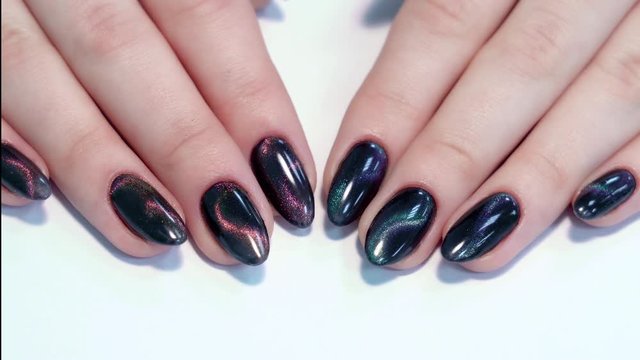 Closeup top view of professional colorful glossy brilliant holiday manicure at fingers of young woman. Modern trendy shiny amazing cat eye effect nail design.
