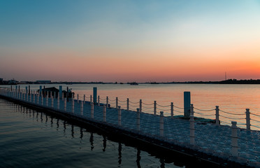 Dark shadow of the sea. The walkway raft is made with many plastic bucket and there is rail. During in the dusk.