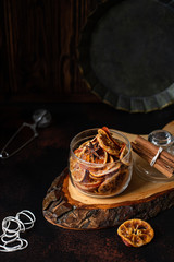 Homemade candied orange slices in a glass jar, orange confiture on a dark table. Dark vintage background, vintage crockery, cinnamon and slices of dried orange. Copy-space, close-up