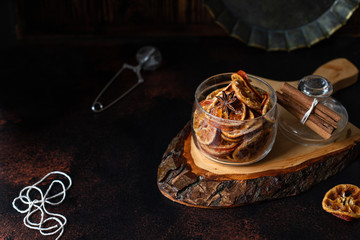 Homemade candied orange slices in a glass jar, orange confiture on a dark table. Dark vintage background, vintage crockery, cinnamon and slices of dried orange. Copy-space, close-up