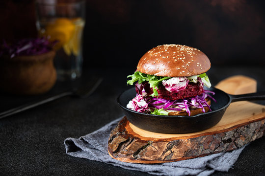 One healthy vegan beetroot burger with red cabbage and lettuce, served in a pan and on a wooden chopping board. Dark background. Close-up. Copy-space