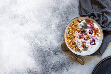 Granola with nuts, greek yogurt, organic jam and chia seeds served in a white bowl and a copper tray. Healthy breakfast, healthy eating concept. Gray background, top view, copy space