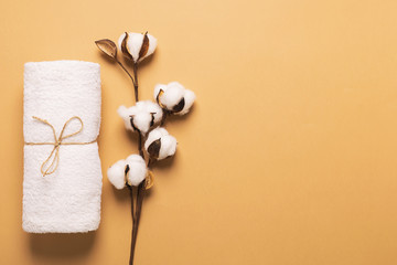 A clean white soft towel is rolled up and tied with a canvas rope with a cotton branch on a brown...