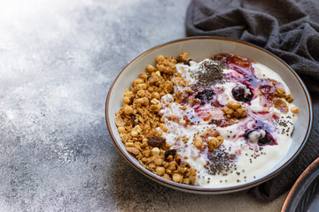 Granola with nuts, greek yogurt, organic jam and chia seeds served in a white bowl and a copper tray. Healthy breakfast, healthy eating concept. Gray background, close up, copy space