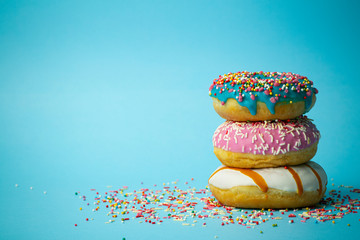 Donuts (doughnuts) of different colors on a blue background with multi-colored festive sugar...