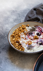 Granola with nuts, greek yogurt, organic jam and chia seeds served in a white bowl and a copper tray. Healthy breakfast, healthy eating concept. Gray background, close up, copy space