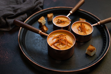Sweet potato cream soup with sweet potato chips, breadcrumbs and herbs served in vintage copper plates on a vintage tray on a dark background. Vegetarian cream soup, healthy food