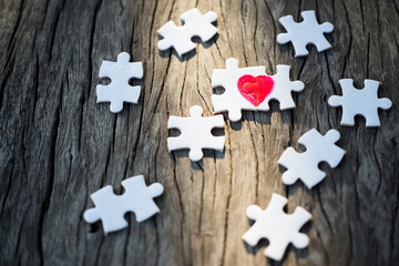 top view of connected jigsaw puzzle pieces with drawn red heart on old wood background. love or...