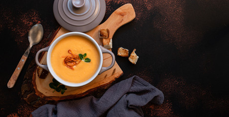Cream sweet potato soup with sweet potato chips, breadcrumbs and herbs served in vintage copper plates on a vintage tray on a dark background. Vegetarian cream soup, healthy food. Top view, copy space