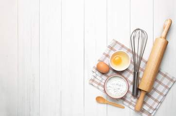 Rolling pin, tapioca flour, egg, oven glove and a whisk on vintage wooden table.