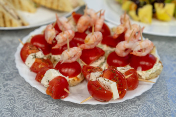 close-up Small sandwiches for the holiday. A plate with many festive snacks for a buffet table. Canape with shrimp, cheese, tomato.