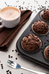 fresh chocolate muffins in muffin tin near brown napkin with coffee