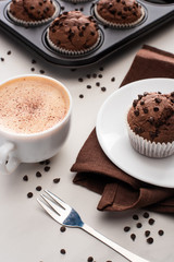 fresh chocolate muffins in muffin tin, brown napkin with plate near coffee and fork