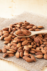 Closeup almonds nut are poured from wooden spoon on sack and table.