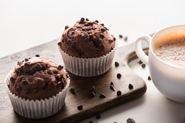 fresh chocolate muffins on wooden cutting board near cappuccino