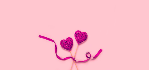 Abstract composition with two decorative hearts with ribbon on pink paper background.