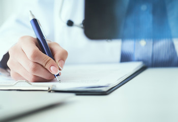 Close up of female doctor holding x-ray or roentgen image and making notes in medical form.