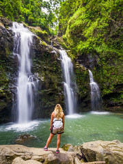 Blonde girl admires Three Bears Falls in Maui, Hawaii Hana Highway - Upper Waikani Falls. Road to...