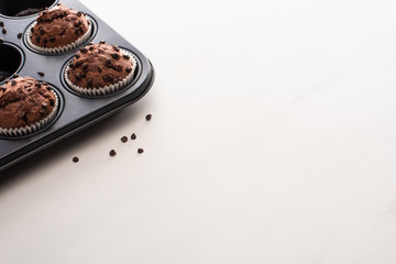 fresh chocolate muffins in muffin tin on white surface