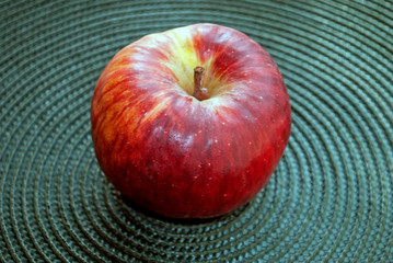 Red apple on a rug. Wicker structure. Dark green background.