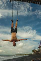 outdoors portrait of young attractive and athletic man practicing aero yoga workoutat the beach...