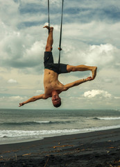outdoors portrait of young attractive and athletic man practicing aero yoga workoutat the beach...