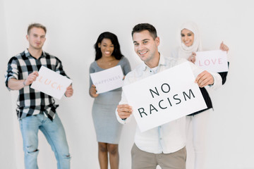 A white man in casual wear holds a poster with the No racism text in his hands, standing on white...
