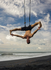 outdoors portrait of young attractive and athletic man practicing aero yoga workoutat the beach...