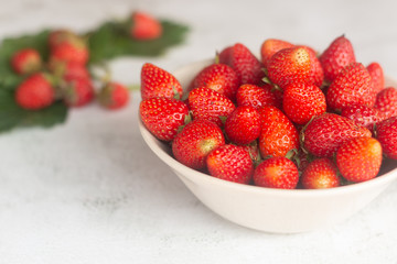 Fresh strawberries with green leave head in a white cup on white marble background.