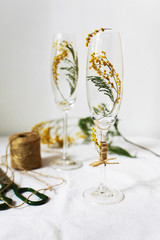 Two tall champagne glasses with branches of mimosa inside. Unusual spring flower arrangement. Beginning of spring, the first flowers. Original design of the festive table for a wedding in spring