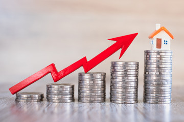 The red arrows on the pile of coins are arranged from low to high and home on the coins. The concept of real estate growth, financial planning, account management and success charts.