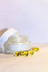Face cream in a gold jar with gold capsules on a light background.