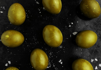 Easter eggs painted in golden yellow monochrome style close up on a black surface with icing...