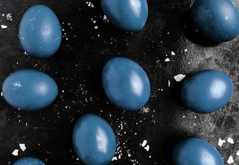 Easter eggs painted in classic blue monochrome style close up on a black surface with icing crumbs....