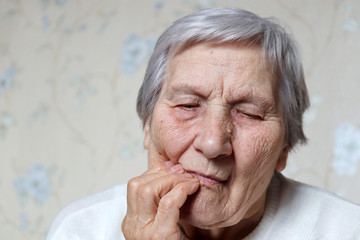 Elderly woman holding her cheek, female with gray hair suffering from a toothache. Concept of tooth pain, gum disease and old age