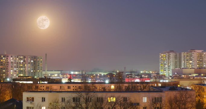 Time lapse of full moon rising over cityscape at sunset, from day to night - fixed angle.